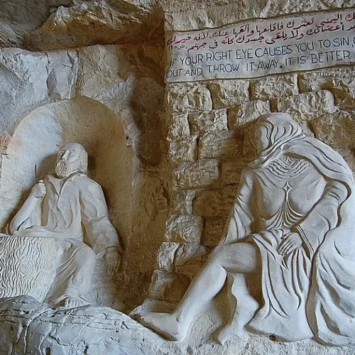 Bas-relief of St. Simon the Tanner at work carved in limestone beside a seated figure and bilingual Gospel inscription