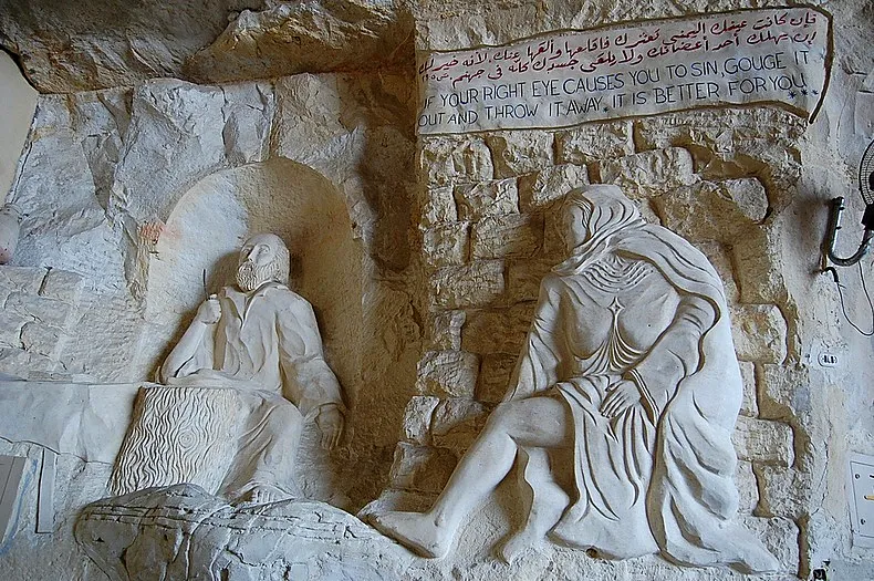 Bas-relief of St. Simon the Tanner at work carved in limestone beside a seated figure and bilingual Gospel inscription