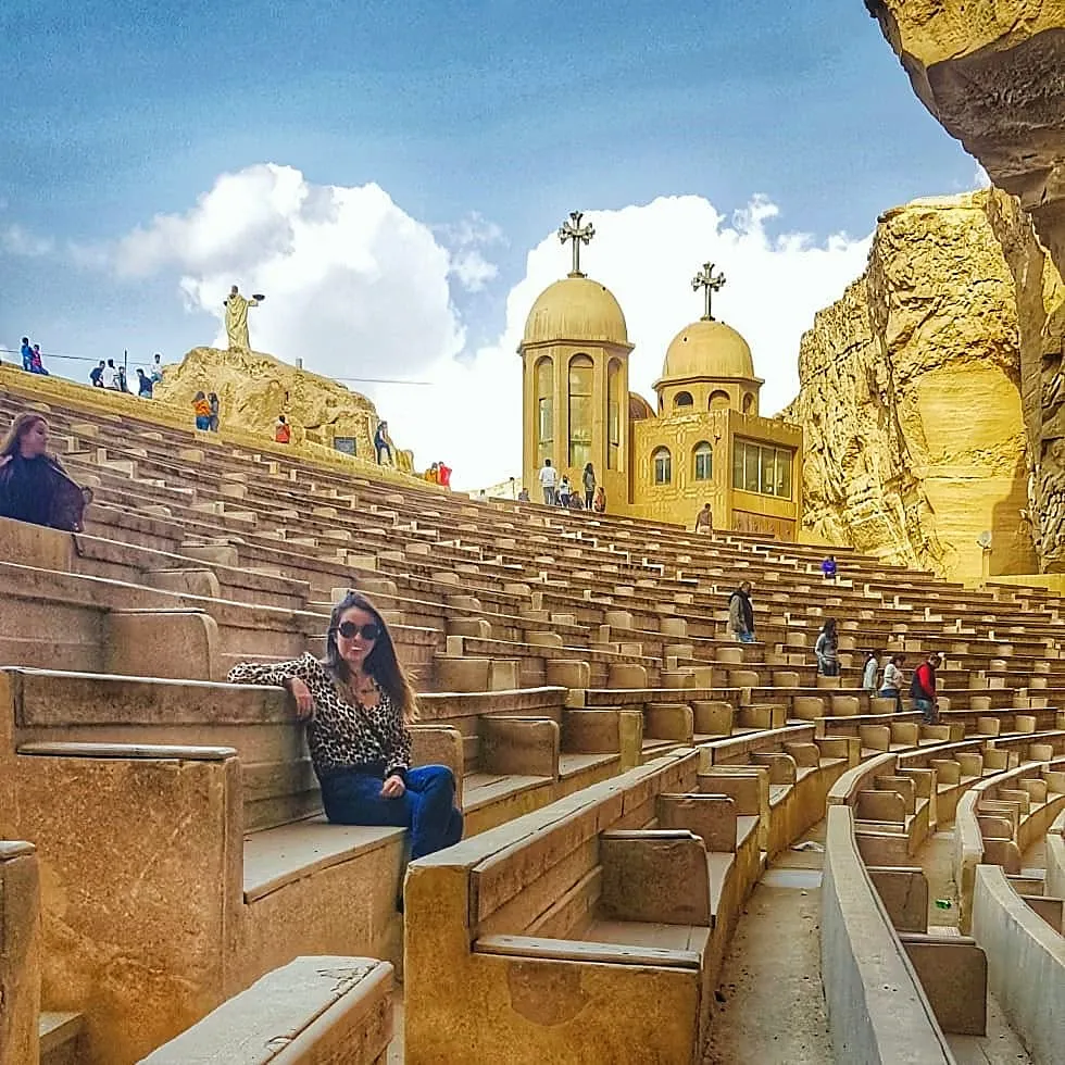 Traveler seated on stone tiers of the St. Simon Cave Church amphitheater in Mokattam with monastery domes behind