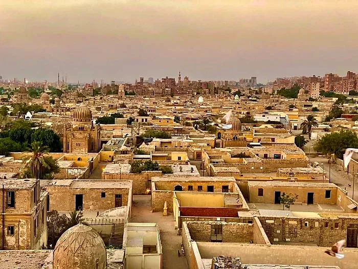 Golden-hour skyline of Cairo’s historic necropolis with ornate Islamic domes and pigeons in flight