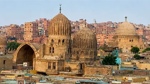 Historic ribbed stone domes and an open iwan in the City of the Dead with modern brick apartments rising behind