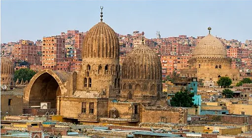 Historic ribbed stone domes and an open iwan in the City of the Dead with modern brick apartments rising behind