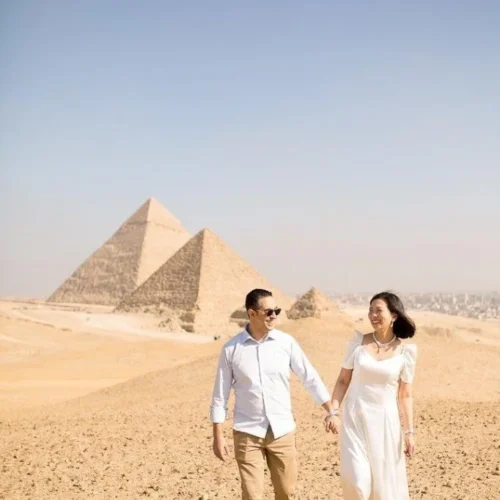 Couple holding hands and smiling while walking on the Giza plateau with the pyramids behind them