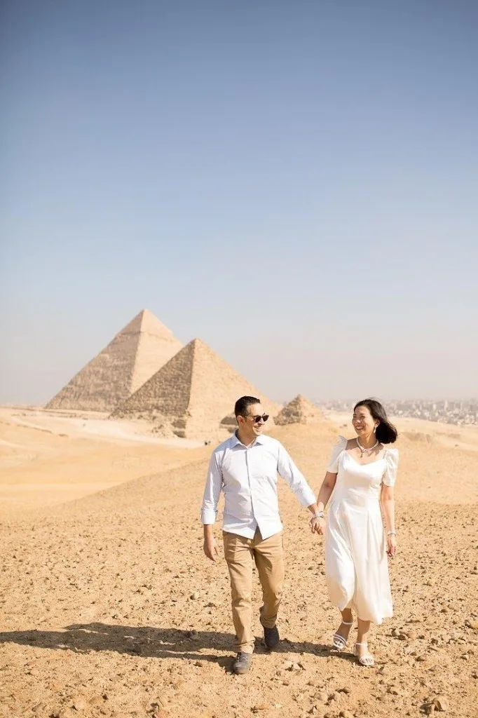 Couple holding hands and smiling while walking on the Giza plateau with the pyramids behind them
