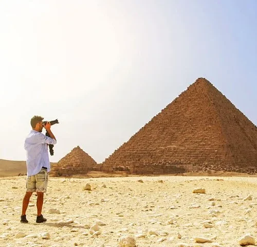 Photographer aiming a DSLR camera toward the Great Pyramids of Giza from the desert plateau