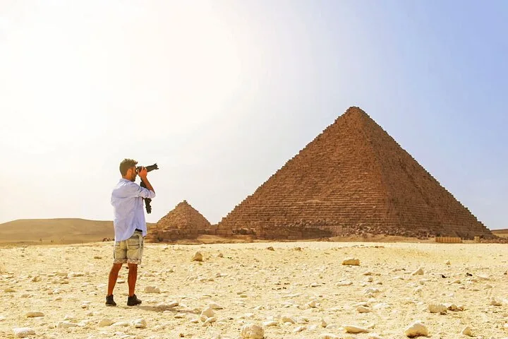 Photographer aiming a DSLR camera toward the Great Pyramids of Giza from the desert plateau