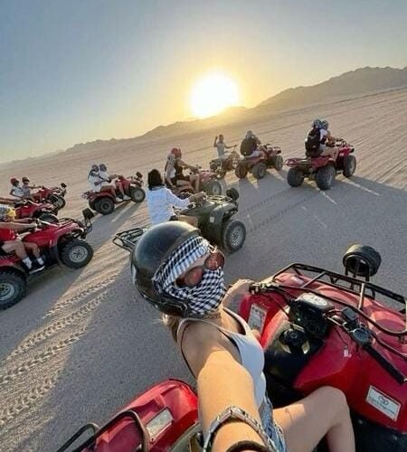 Traveler selfie on a red quad bike leading a convoy across desert sand toward sunset near Hurghada