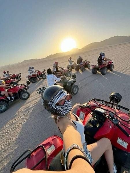 Traveler selfie on a red quad bike leading a convoy across desert sand toward sunset near Hurghada