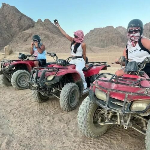 Three travelers on red quad bikes in the desert mountains near Hurghada, wearing helmets and keffiyehs