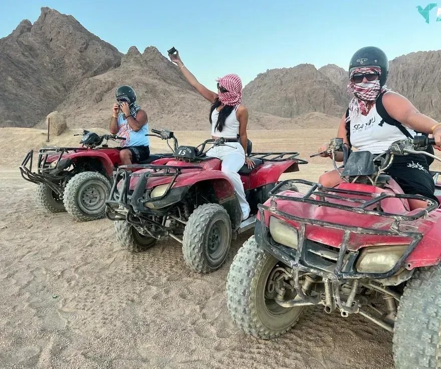 Three travelers on red quad bikes in the desert mountains near Hurghada, wearing helmets and keffiyehs