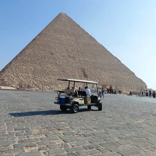 Beige golf cart on stone pavement below the Great Pyramid of Giza