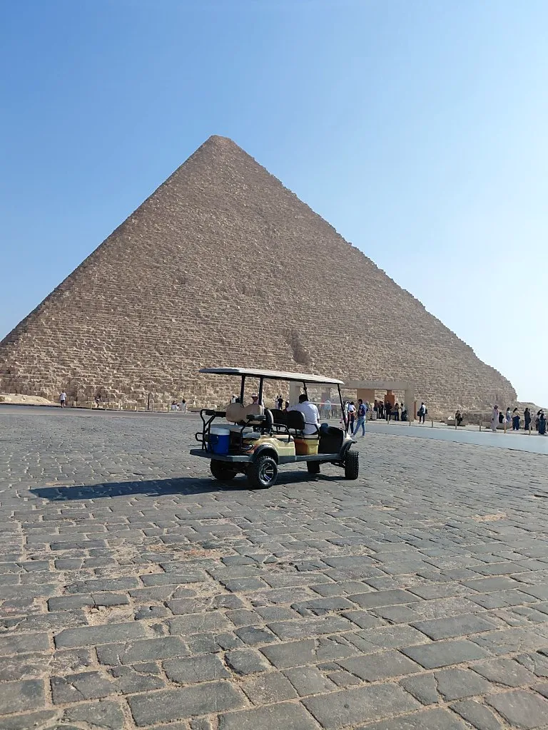 Beige golf cart on stone pavement below the Great Pyramid of Giza