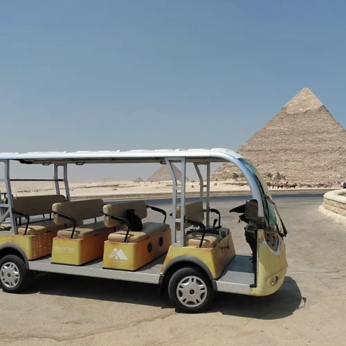 Yellow electric golf cart shuttle parked on the Giza Plateau with the Great Pyramid behind it