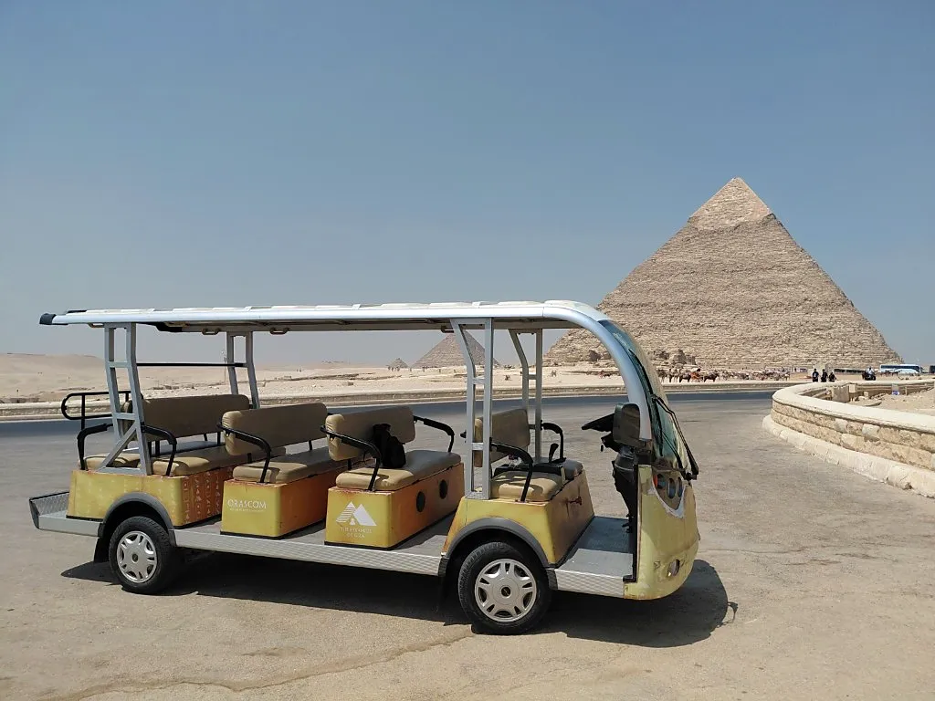 Yellow electric golf cart shuttle parked on the Giza Plateau with the Great Pyramid behind it