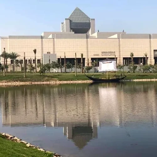 National Museum of Egyptian Civilization in Fustat, Cairo, reflected in Ain El-Sira Lake with a traditional boat in the foreground