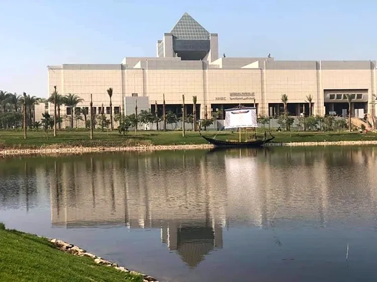 National Museum of Egyptian Civilization in Fustat, Cairo, reflected in Ain El-Sira Lake with a traditional boat in the foreground
