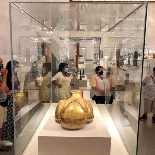 Travelers gathered around a golden sarcophagus fragment in a tall glass case at NMEC