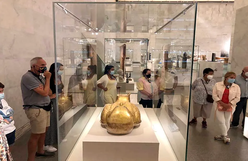 Travelers gathered around a golden sarcophagus fragment in a tall glass case at NMEC