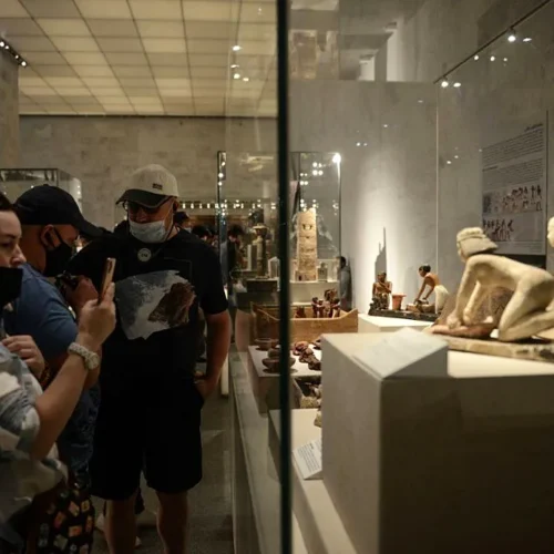Travelers photographing ancient Egyptian figurines inside a glass display case at NMEC Cairo