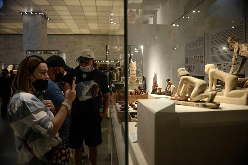 Travelers photographing ancient Egyptian figurines inside a glass display case at NMEC Cairo