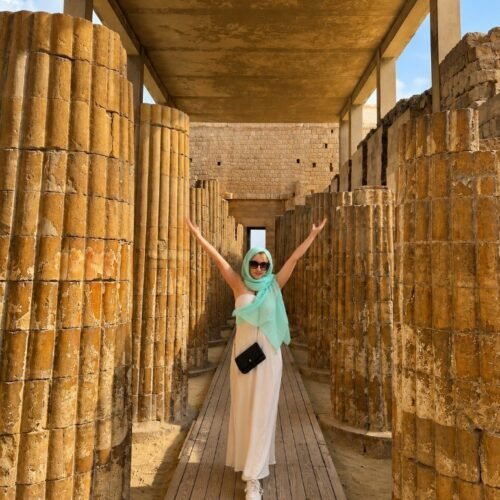 Traveler in a white dress raising both arms between the fluted stone columns of the Djoser colonnade at Saqqara