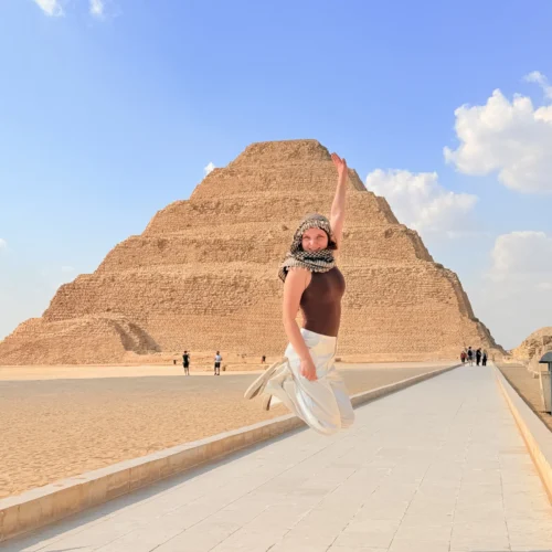 Traveler jumping on a paved walkway in front of the Step Pyramid of Djoser at Saqqara