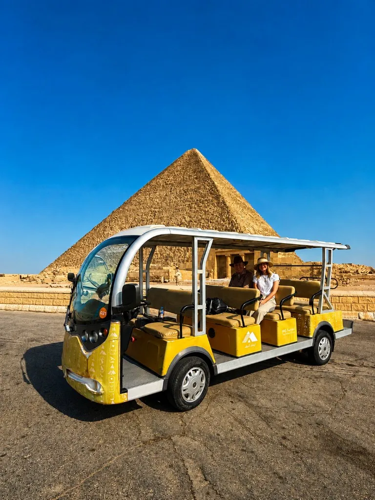 Official yellow plateau shuttle parked on the asphalt with the Great Pyramid rising behind it under a clear blue sky