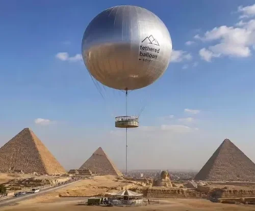 Silver tethered balloon labeled tethered balloon Egypt above the Giza Pyramids and Great Sphinx
