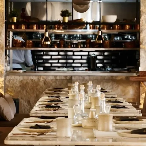 Long indoor dining table at Khufu Restaurant facing an open kitchen with copper pans