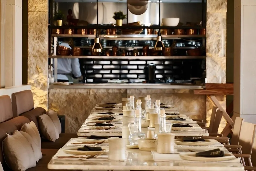 Long indoor dining table at Khufu Restaurant facing an open kitchen with copper pans