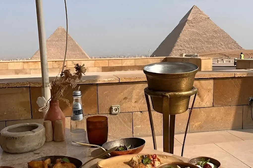 Close table setting of mezze bowls at Khufu Restaurant with two Giza pyramids beyond the limestone terrace wall