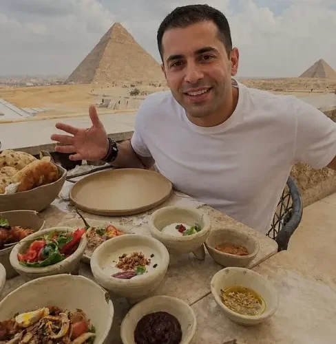 Smiling traveler at a Khufu Restaurant table of Egyptian mezze with the Great Pyramid behind him