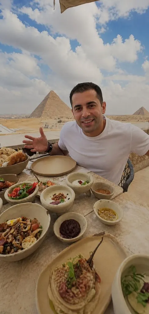 Smiling traveler at a Khufu Restaurant table of Egyptian mezze with the Great Pyramid behind him