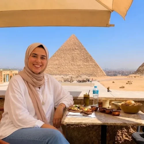 Traveler in a pink hijab dining on the Khufu Restaurant terrace with Khufu and Khafre pyramids in the background