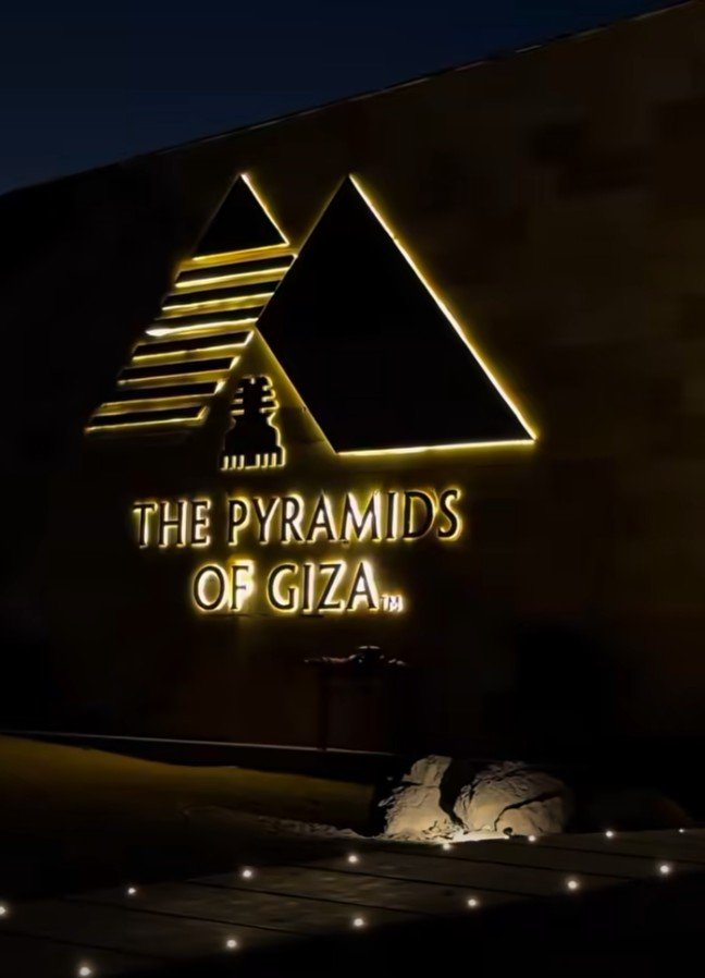 The illuminated sign reading The Pyramids of Giza on a stone wall at night.